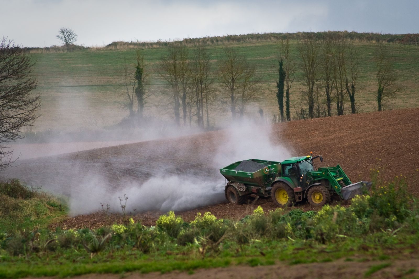 Landwirt der sein Feld mit einem Traktor und Anhänger kalkt